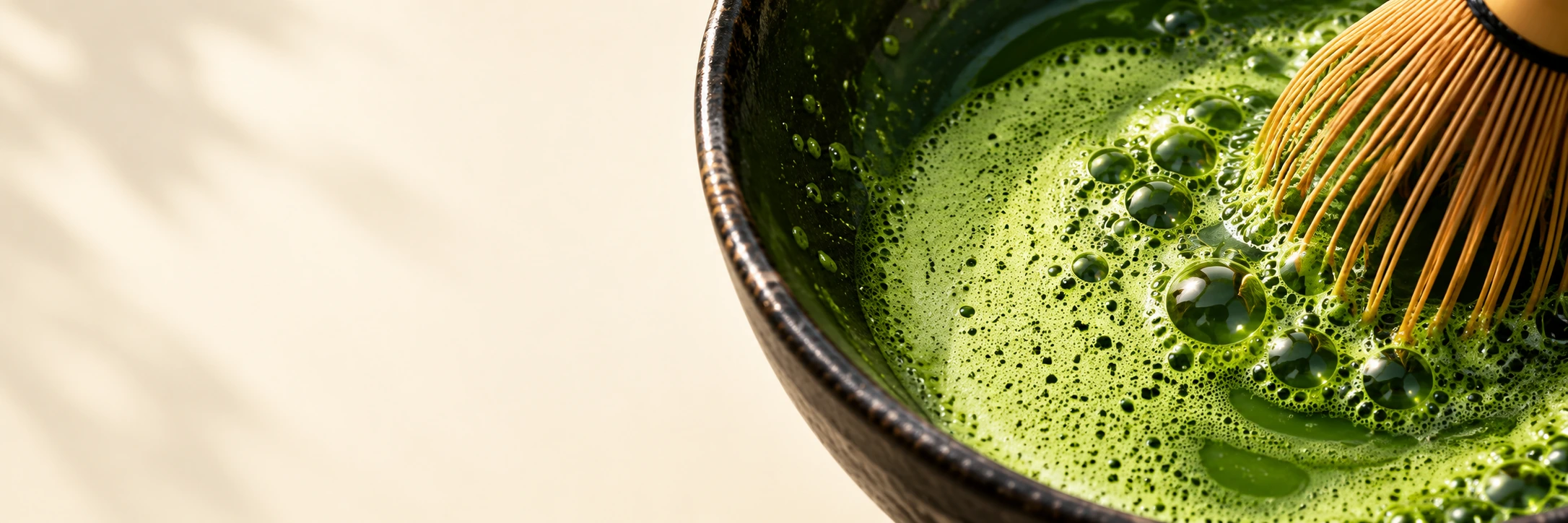 Bright green matcha foam and a bamboo whisk